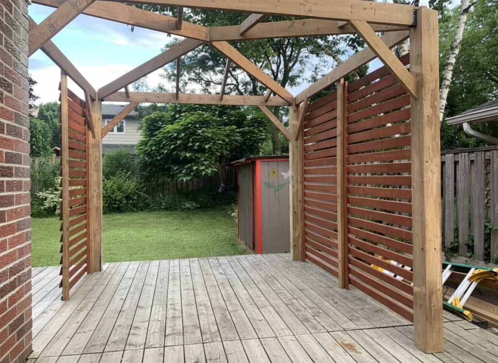 Wooden pergola structure with slatted privacy walls on a backyard deck.
