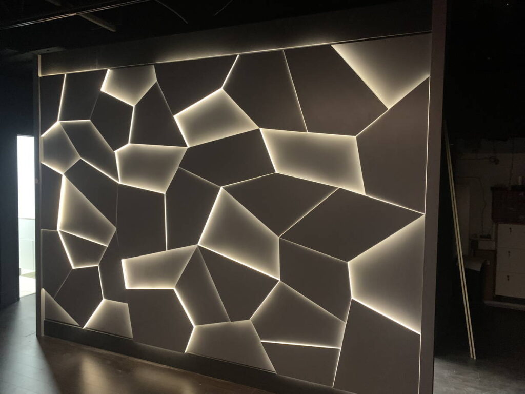 Feature wall with geometric panels and integrated backlighting in a dark interior space.