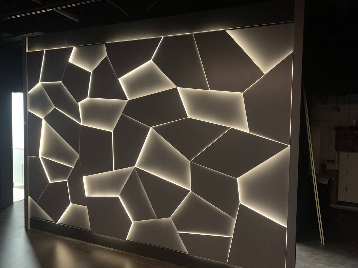 Feature wall with geometric panels and integrated backlighting in a dark interior space.