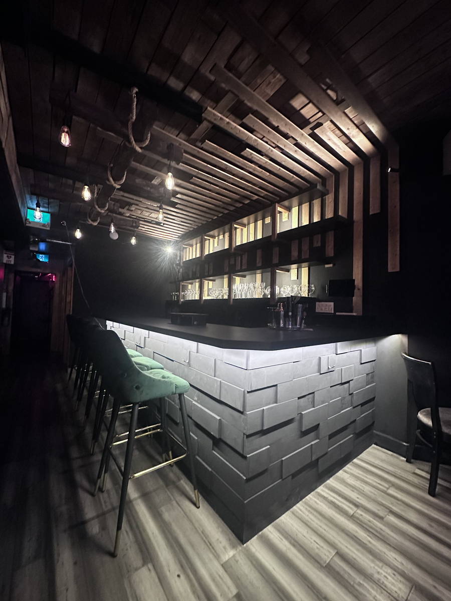 Rustic industrial bar with wood ceiling beams, backlit geometric wall, and green stools.